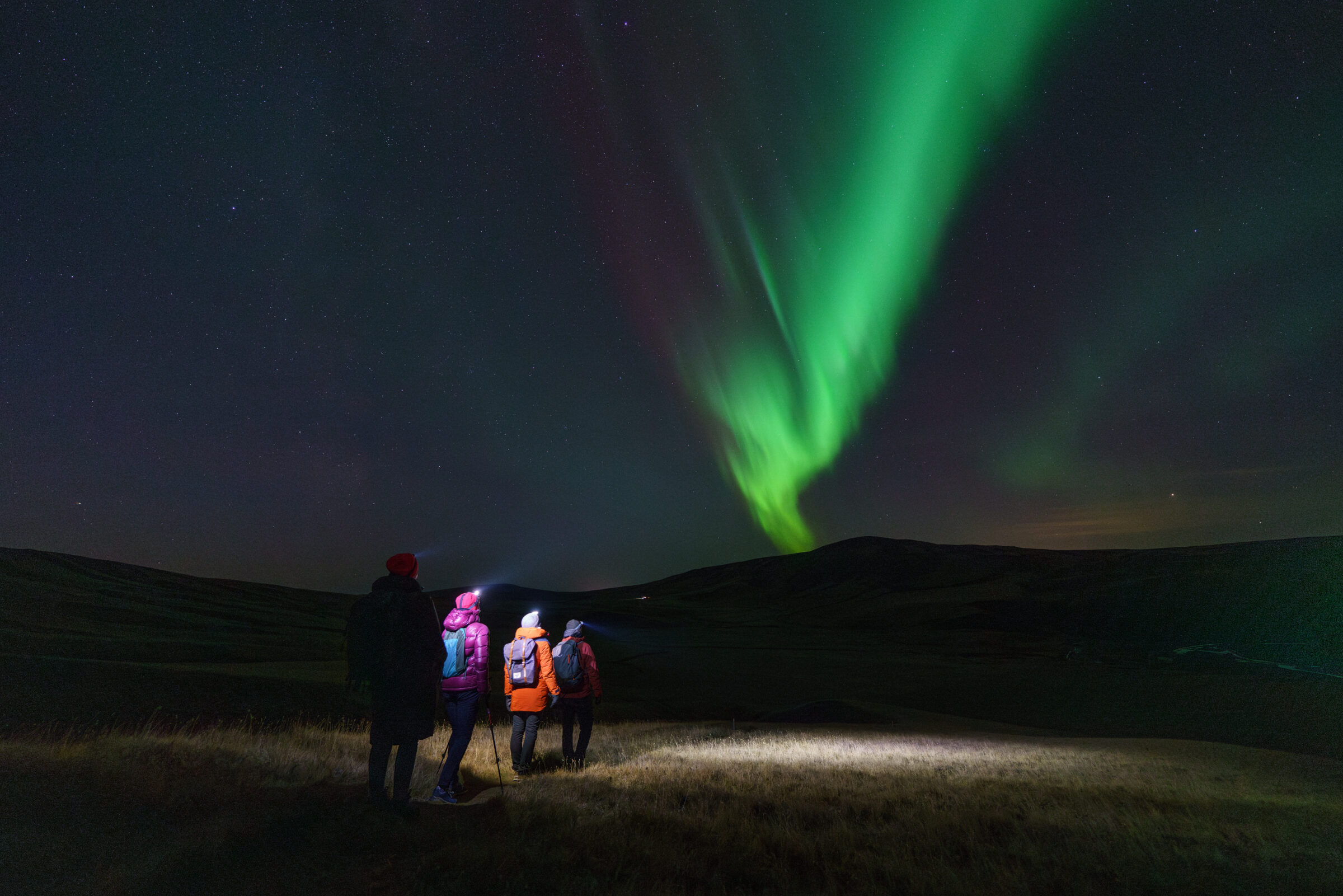 People hiking in the night with Northern Lights in front